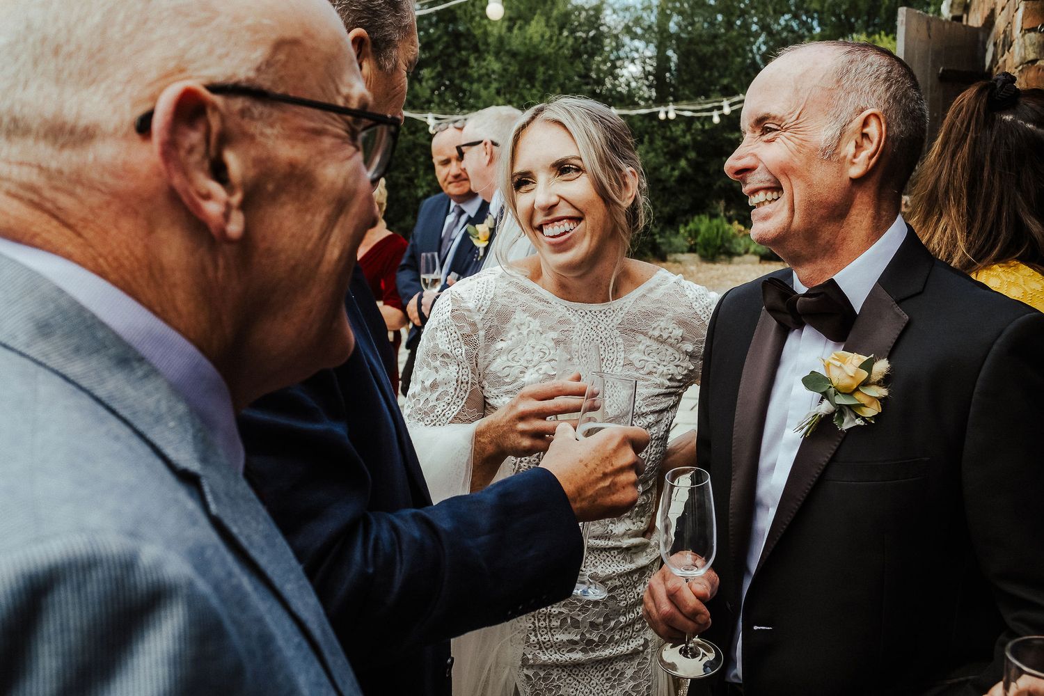 Wedding couple and guests laughing joyfully during outdoor reception celebrations.