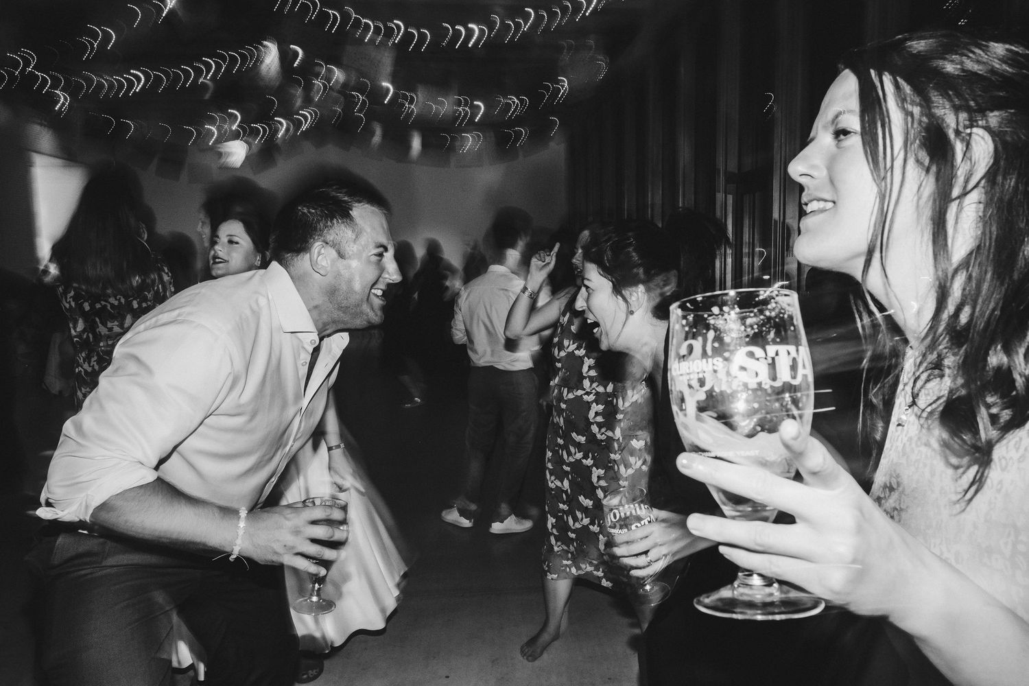 Party guests laugh and interact while holding drinks at a festive celebration.