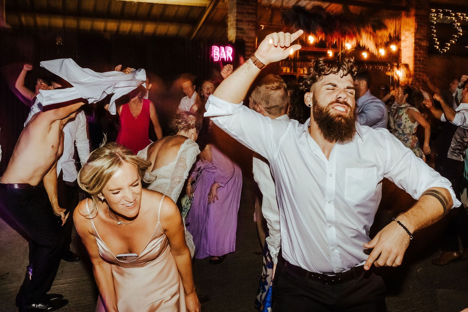 Wedding guests dance energetically on the dance floor during a lively reception celebration.