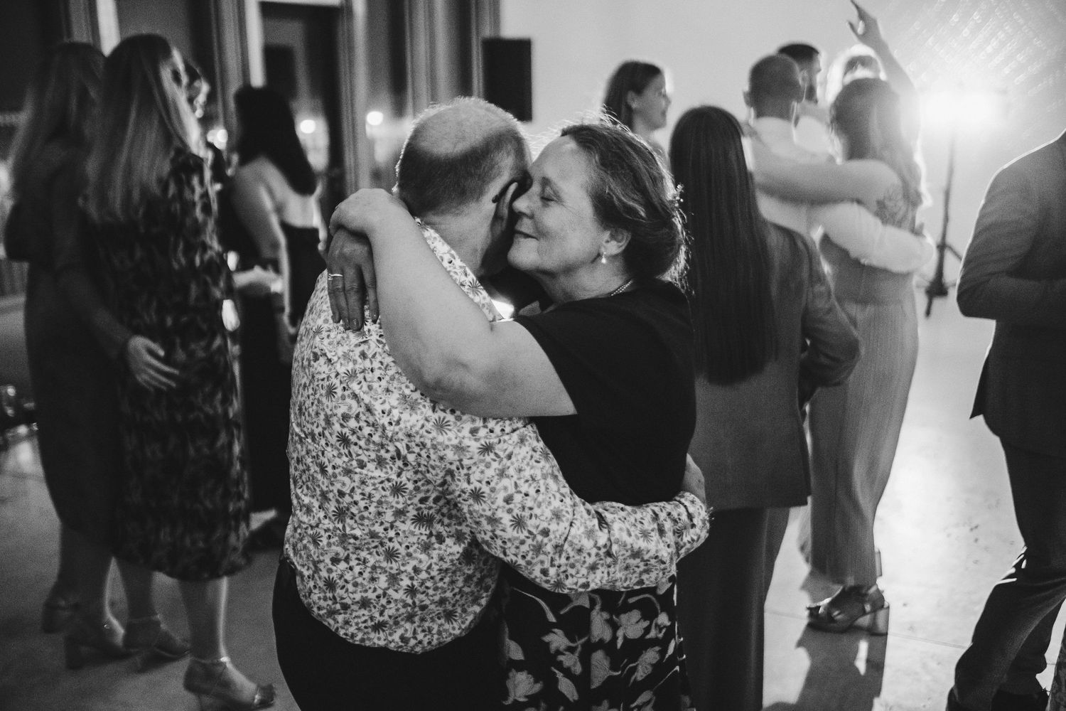 Wedding guests share warm embrace during reception dance.