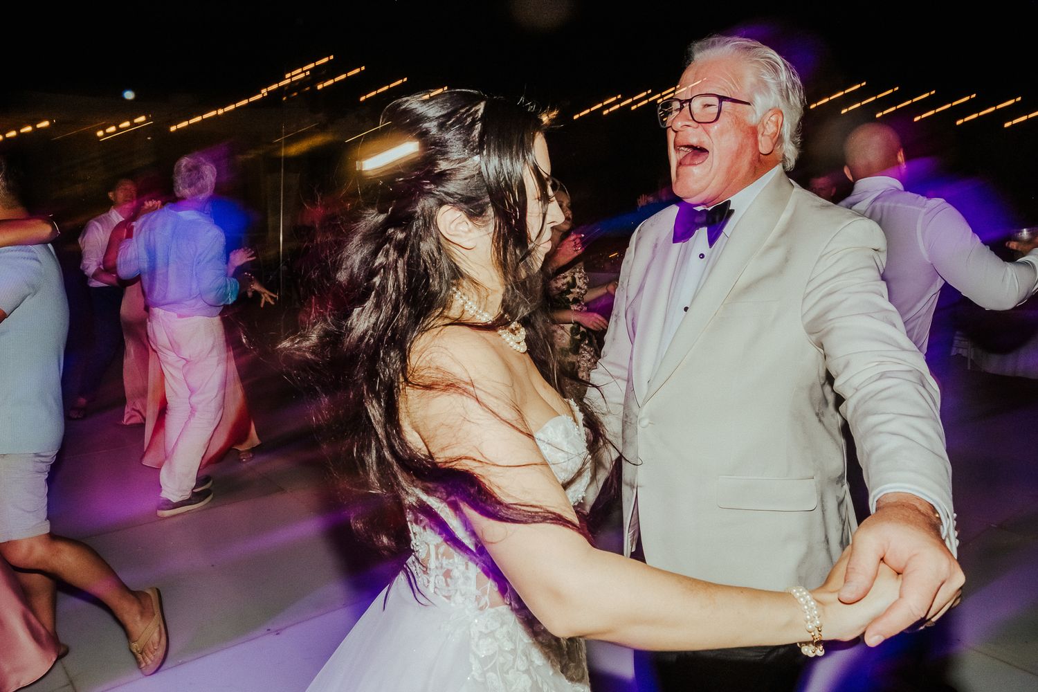 Party guests dancing under purple mood lighting at a nighttime celebration.