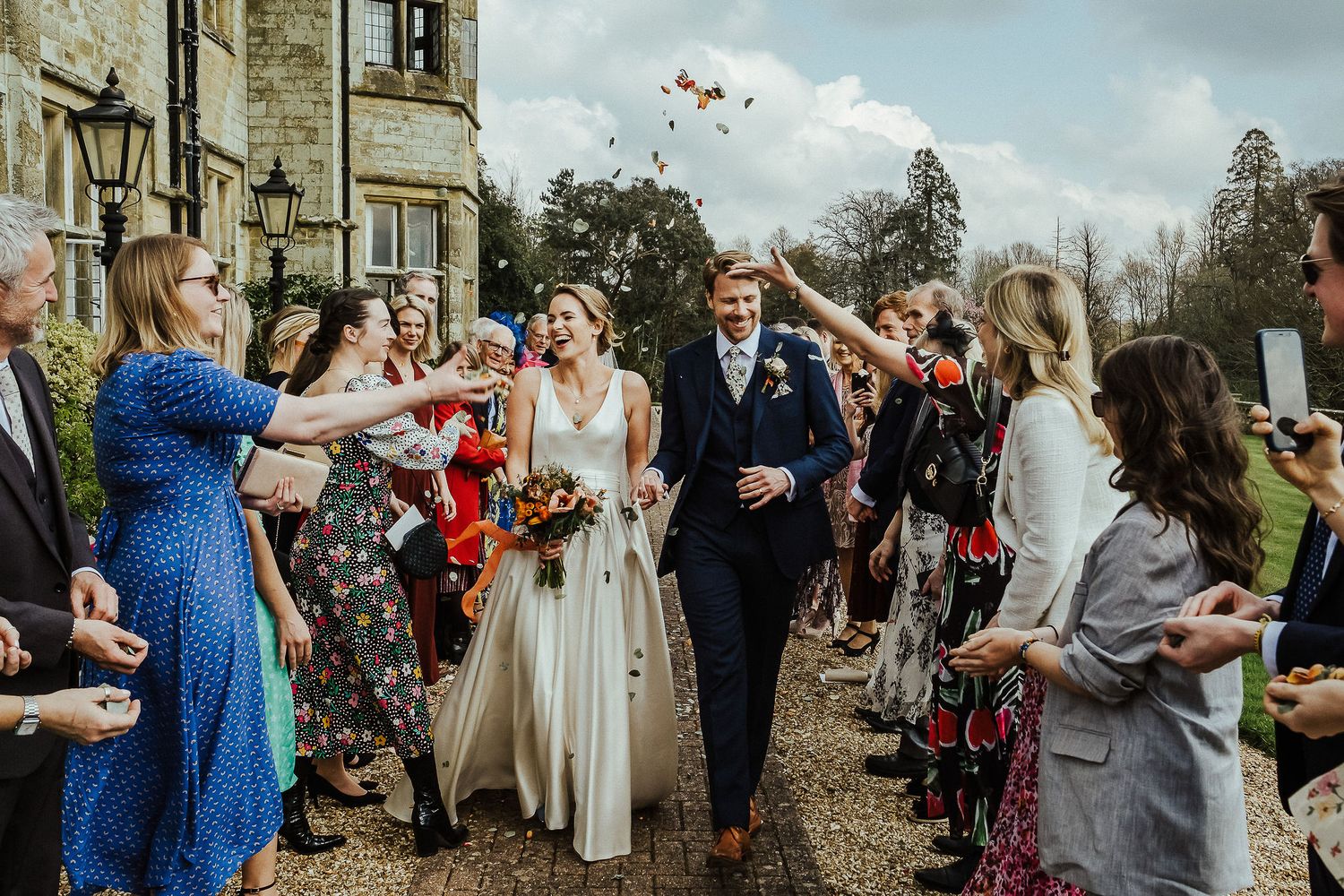 Wedding guests throwing confetti over newlyweds outside stone building.