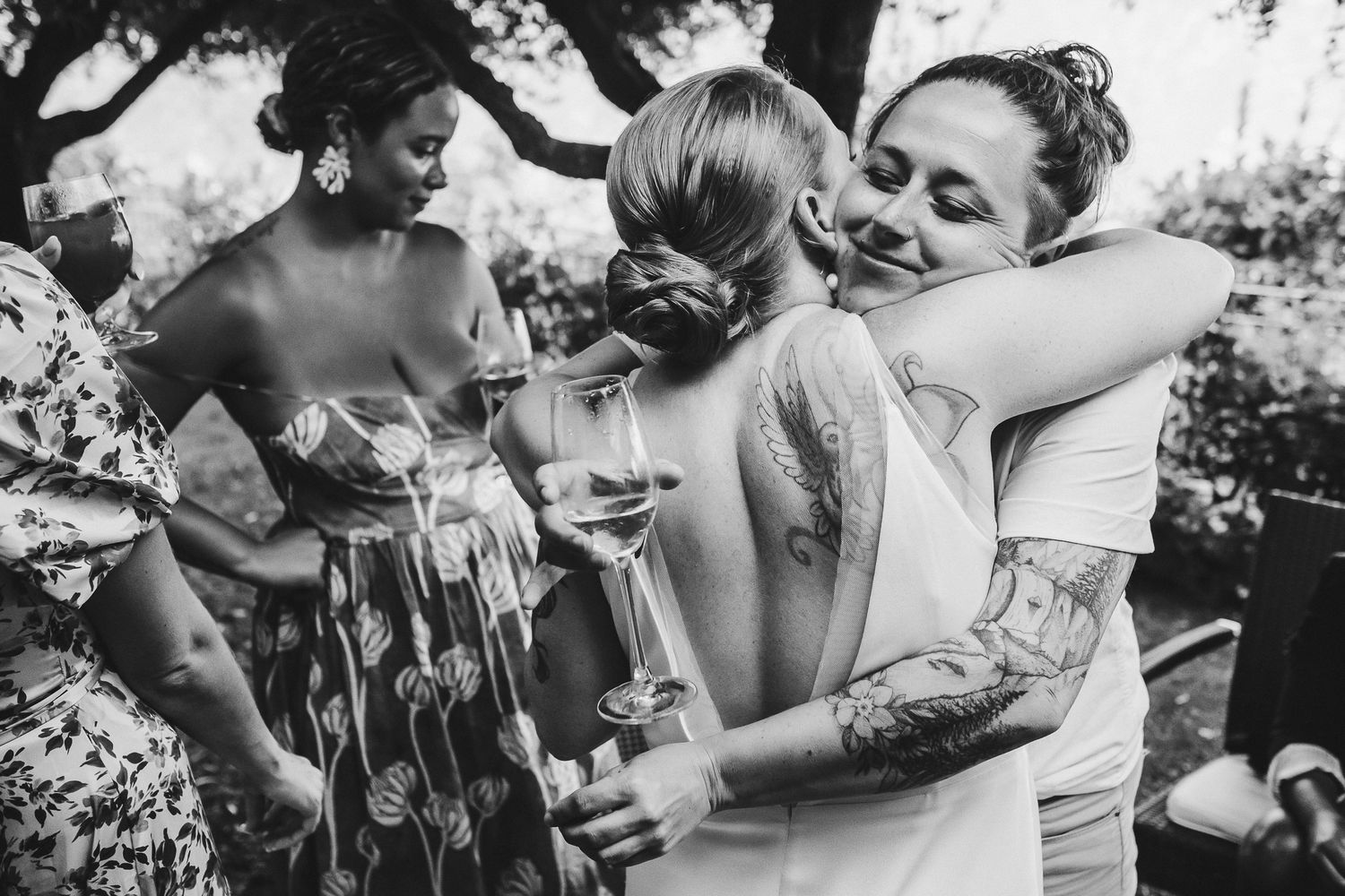 Wedding guests embracing and celebrating with drinks at an outdoor garden party.