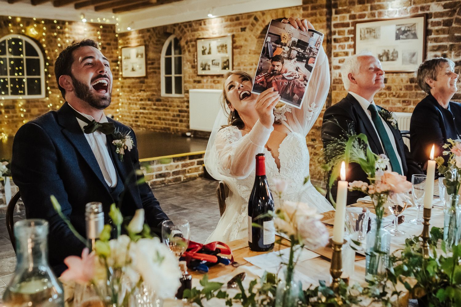 Wedding guests laughing and celebrating with drinks at decorated reception table.