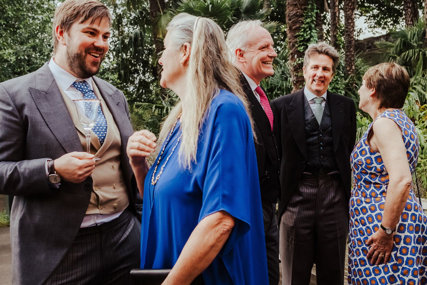 Wedding guests in formal attire gather outdoors during a celebration.