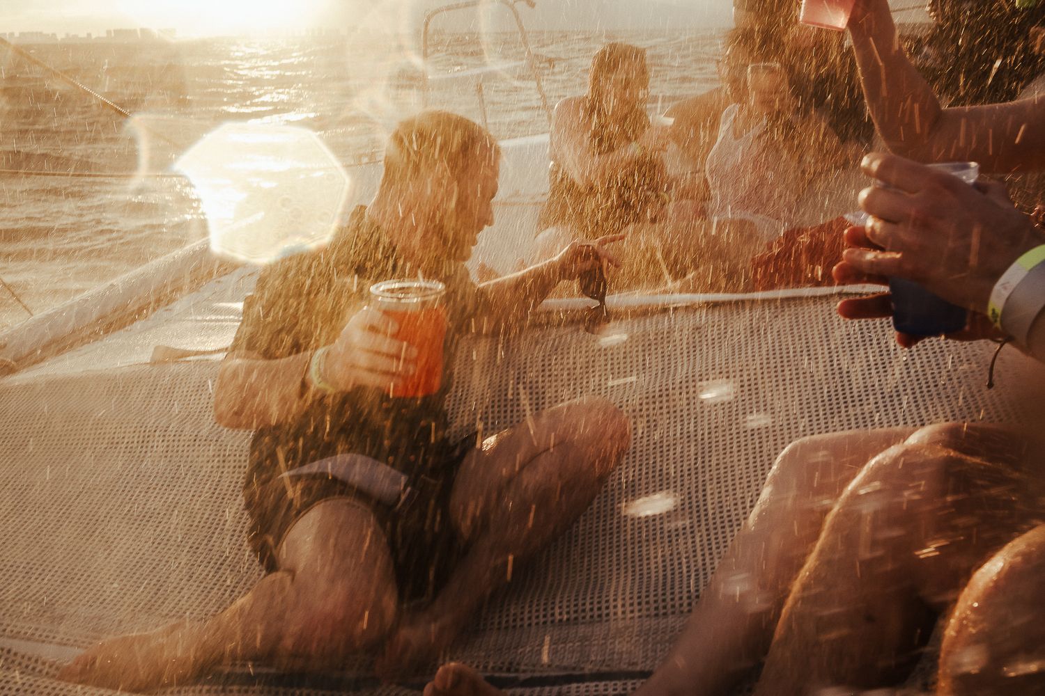Sun-drenched silhouettes of people enjoying drinks on a boat deck at golden hour.
