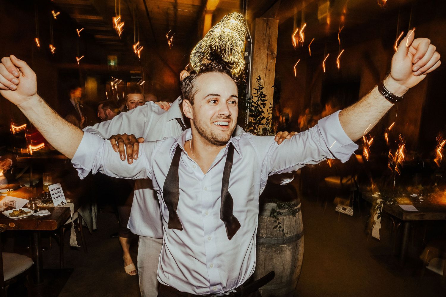 Energetic guest celebrating with arms raised at dimly lit wedding reception.
