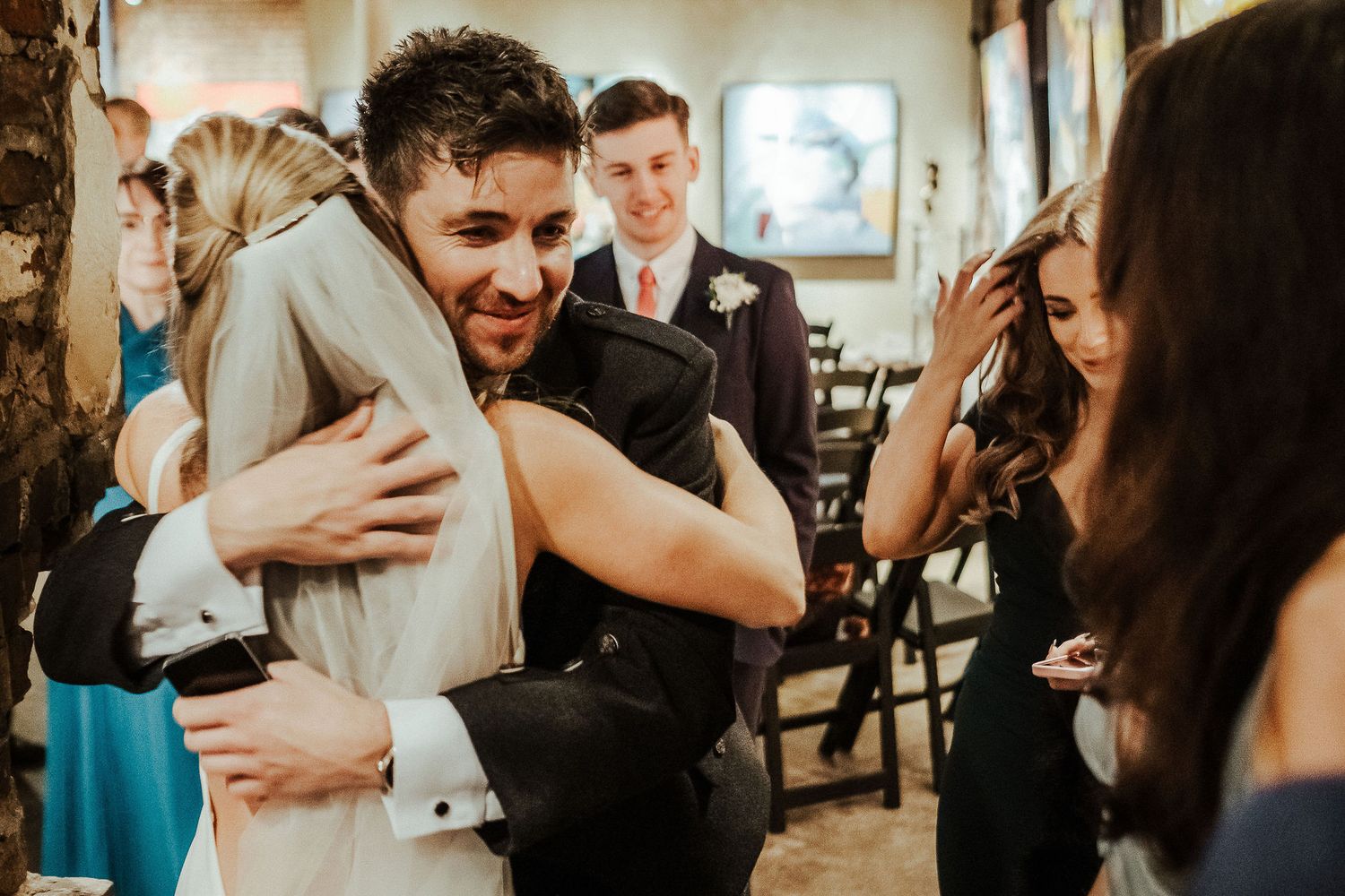 Emotional embrace during wedding reception in warmly lit indoor venue.