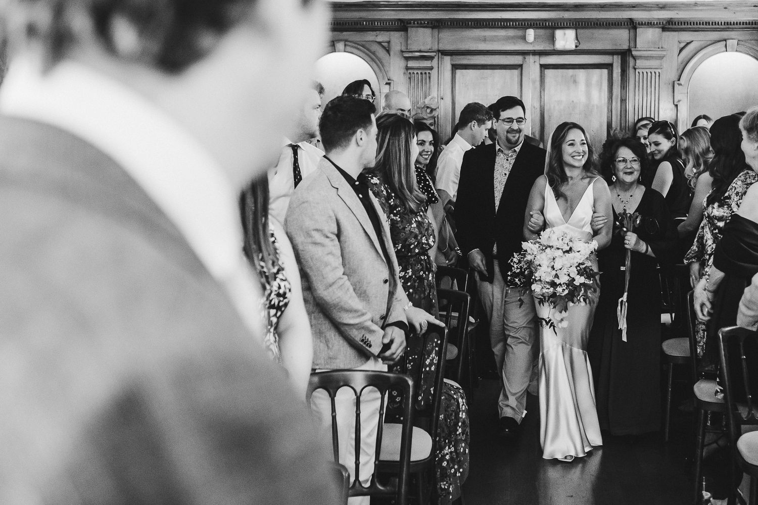 Black and white photo of wedding guests gathered indoors with balloons and flowers.