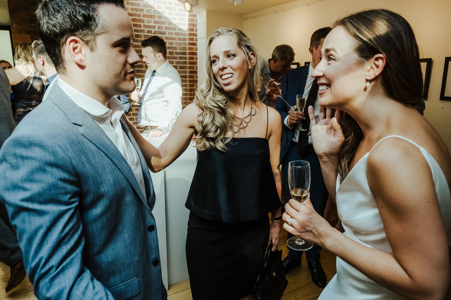 Party guests share animated conversation over champagne at an indoor event.