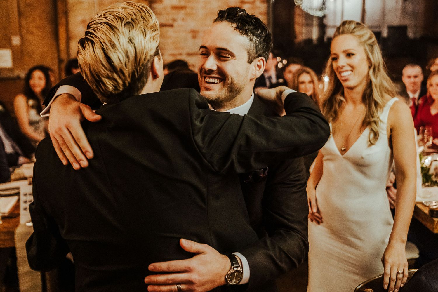 Emotional wedding moment captured as guests embrace during reception celebration.
