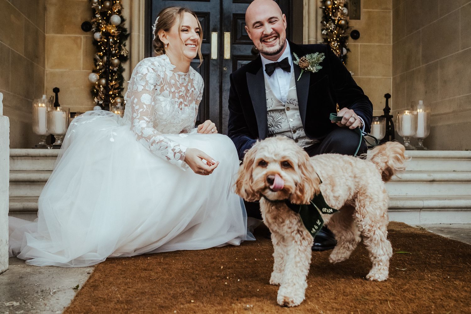 Newlyweds pose on mansion steps with their fluffy dog in formal attire.