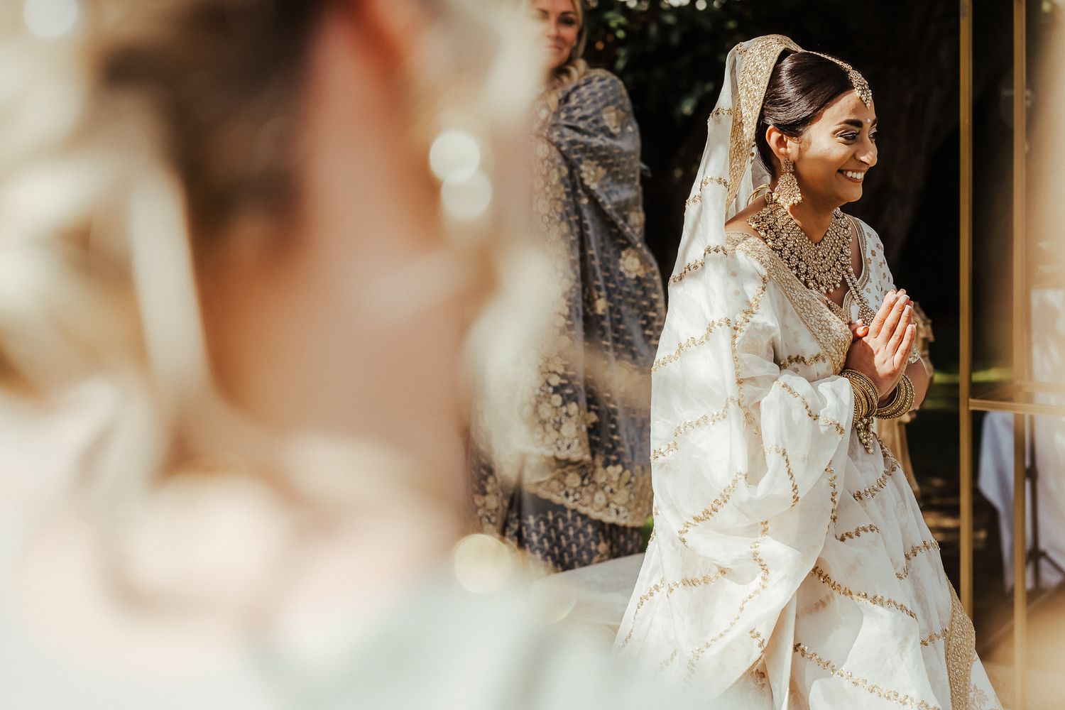 Indian bride in traditional white wedding attire prays with hands clasped before ceremony.