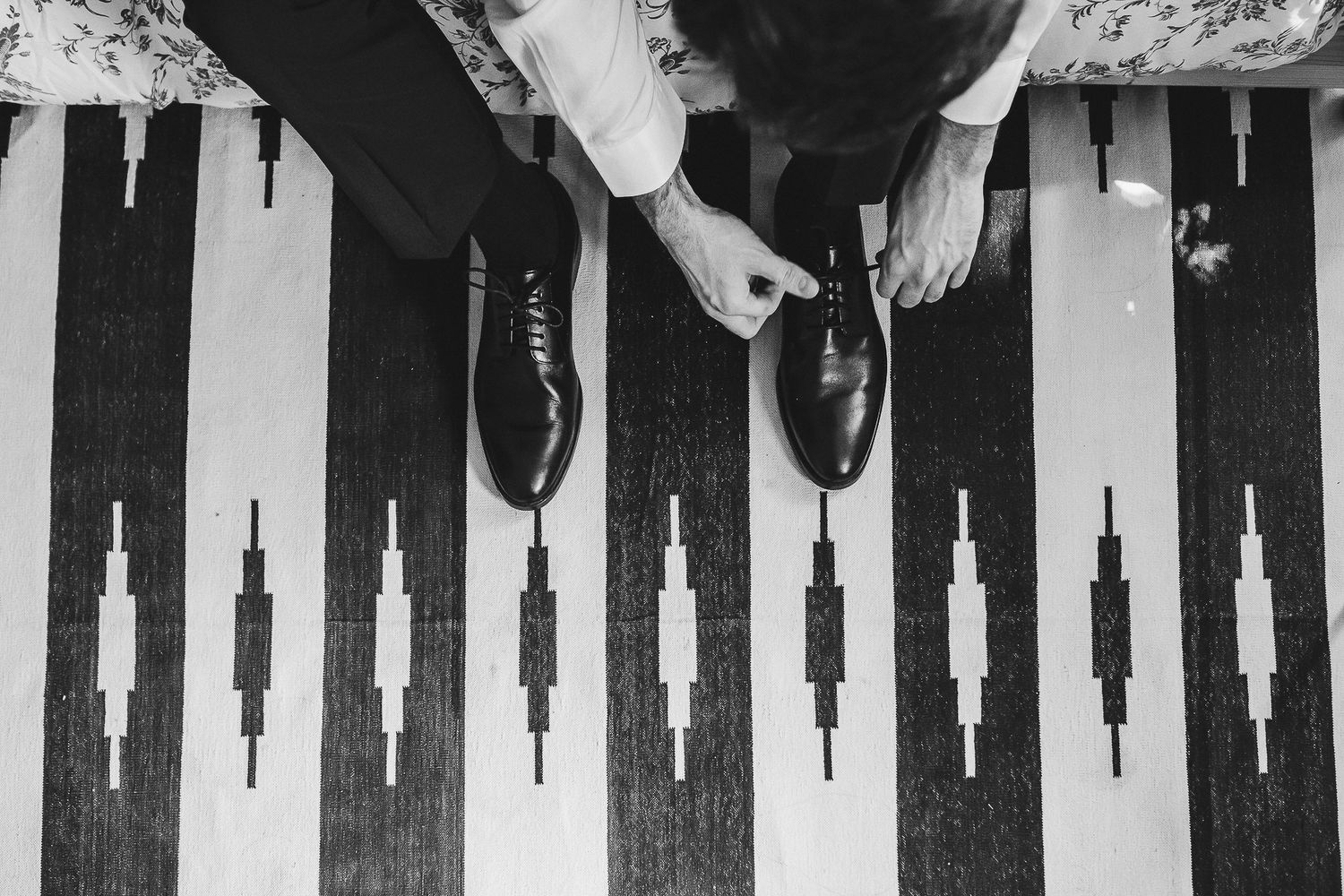 Monochrome overhead view of black dress shoes on a large black and white geometric pattern backgammon board.