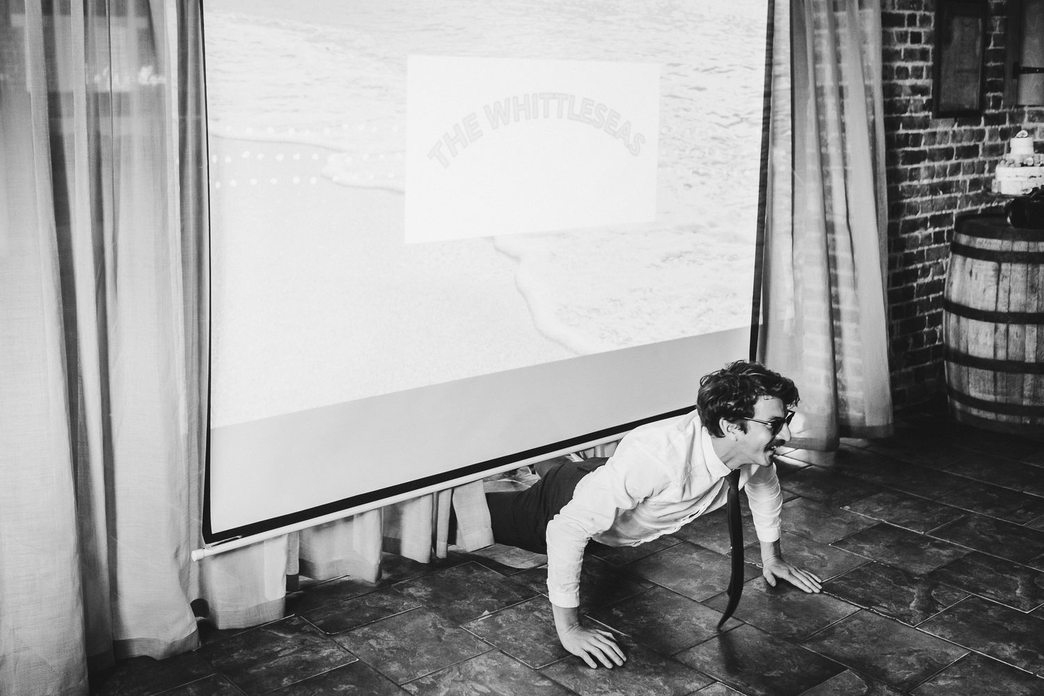 Playful black and white photo of wedding guest crouching near projection screen.