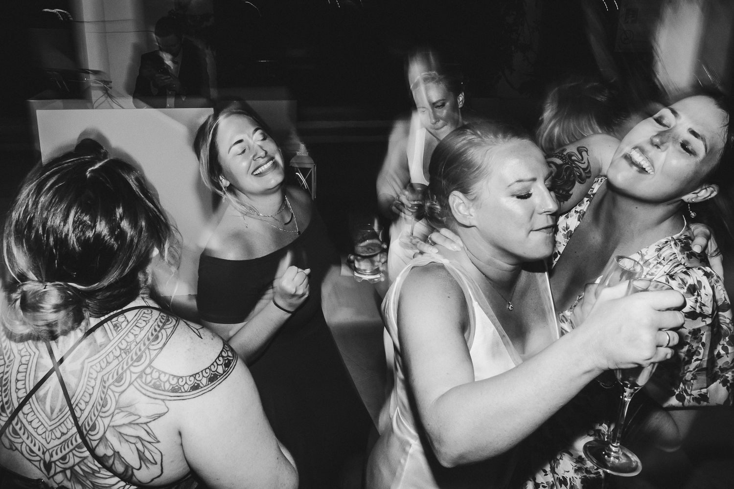 Candid black and white shot of guests laughing and dancing at a celebration.
