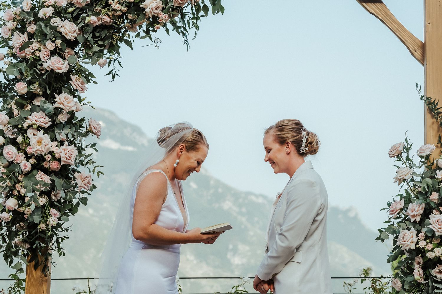 Couple exchanges vows under a floral arch with mountain views.