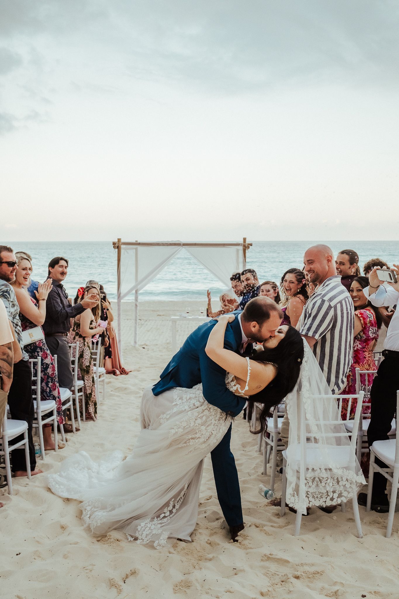 Joyful wedding ceremony finale with couple's dramatic dip kiss on beach.