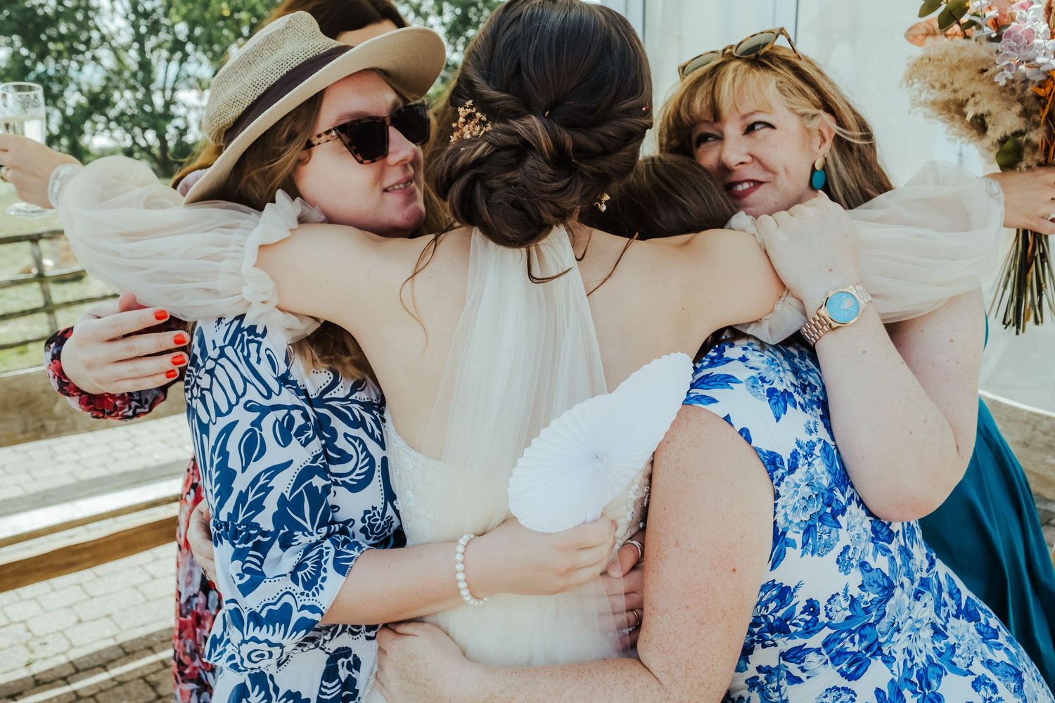 Three women in blue floral dresses sharing an emotional group hug.