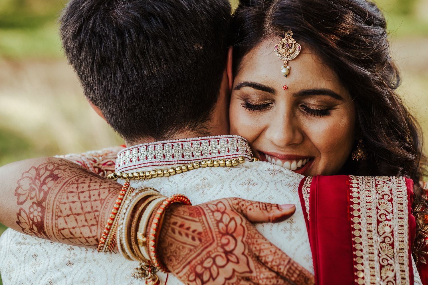 Close-up of newlyweds embracing, showing intricate henna designs and traditional Indian wedding jewelry.