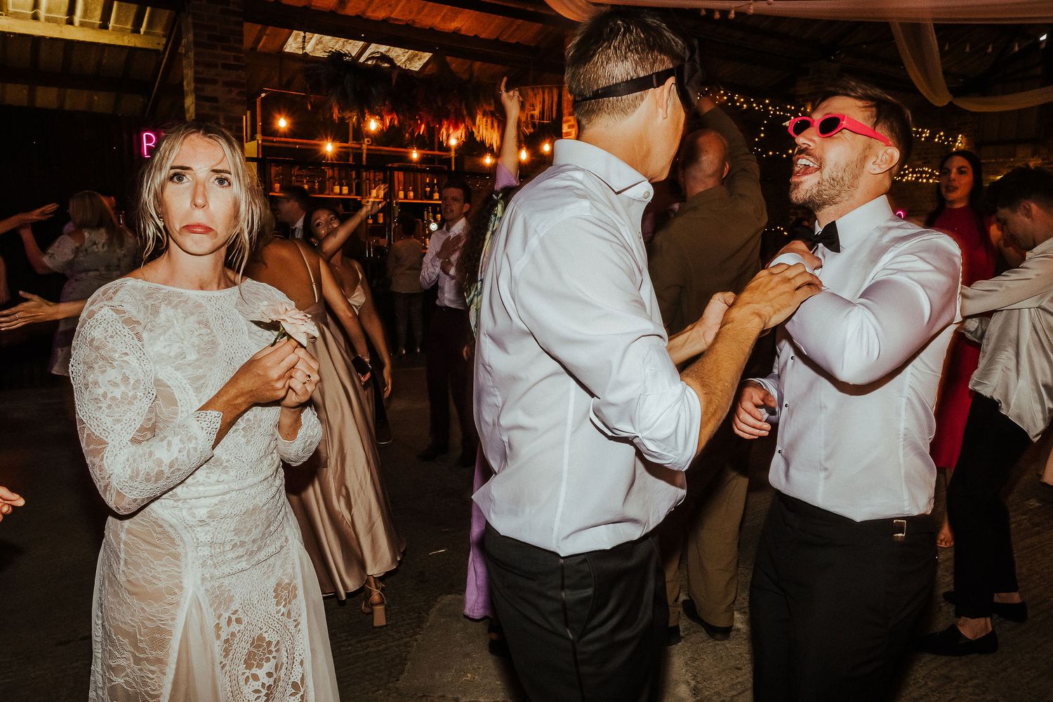 Wedding guests dancing energetically in a rustic venue with atmospheric lighting.