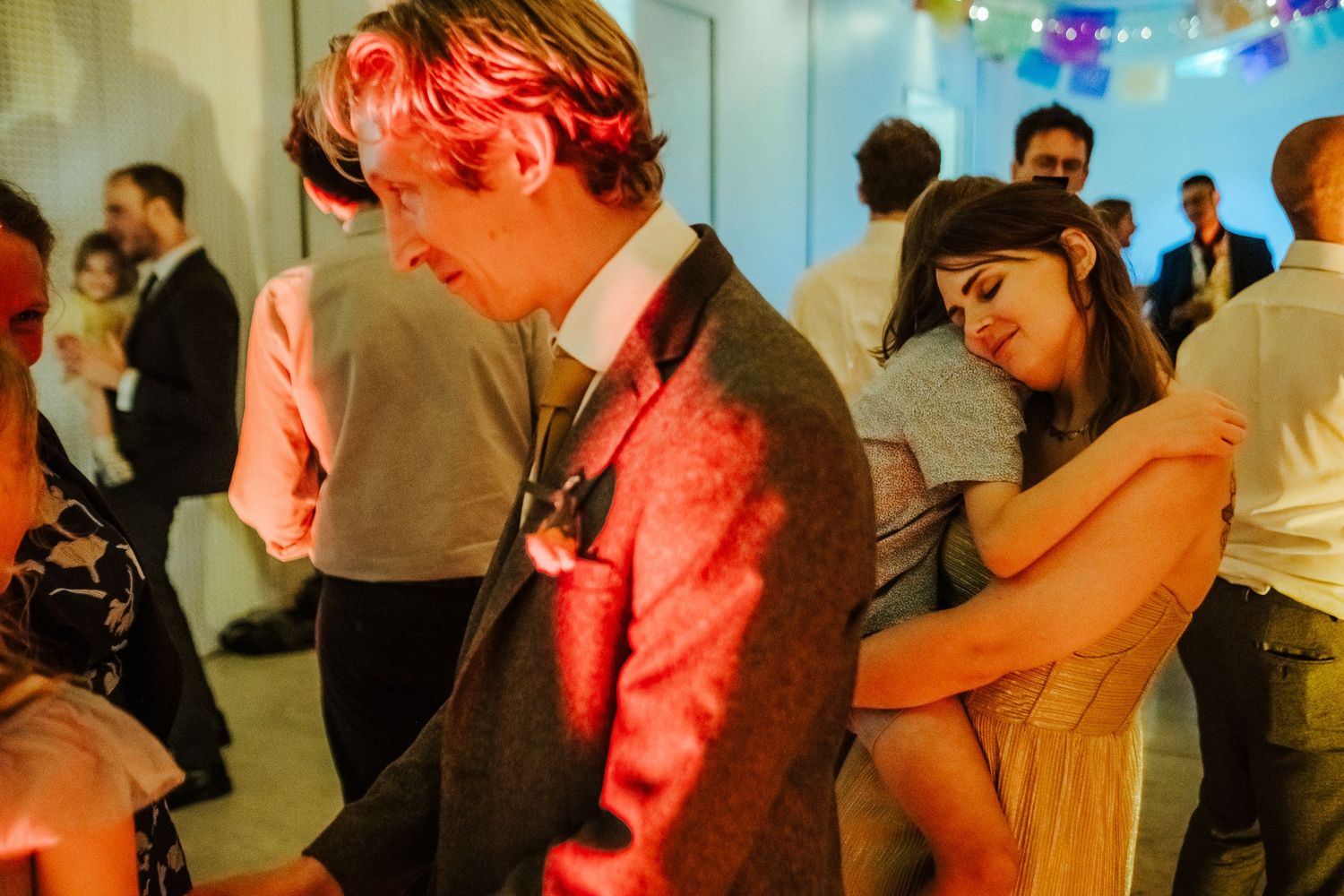 Couples dance closely under colorful party lights at an evening celebration.