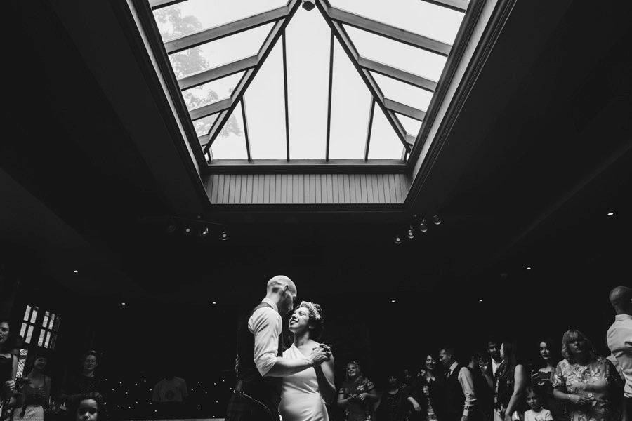 A couple sharing a dance under a dramatic skylight in a dimly lit venue.