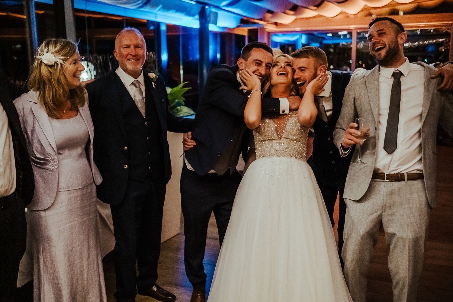 Wedding party shares a joyful moment together at a reception with colorful ambient lighting.