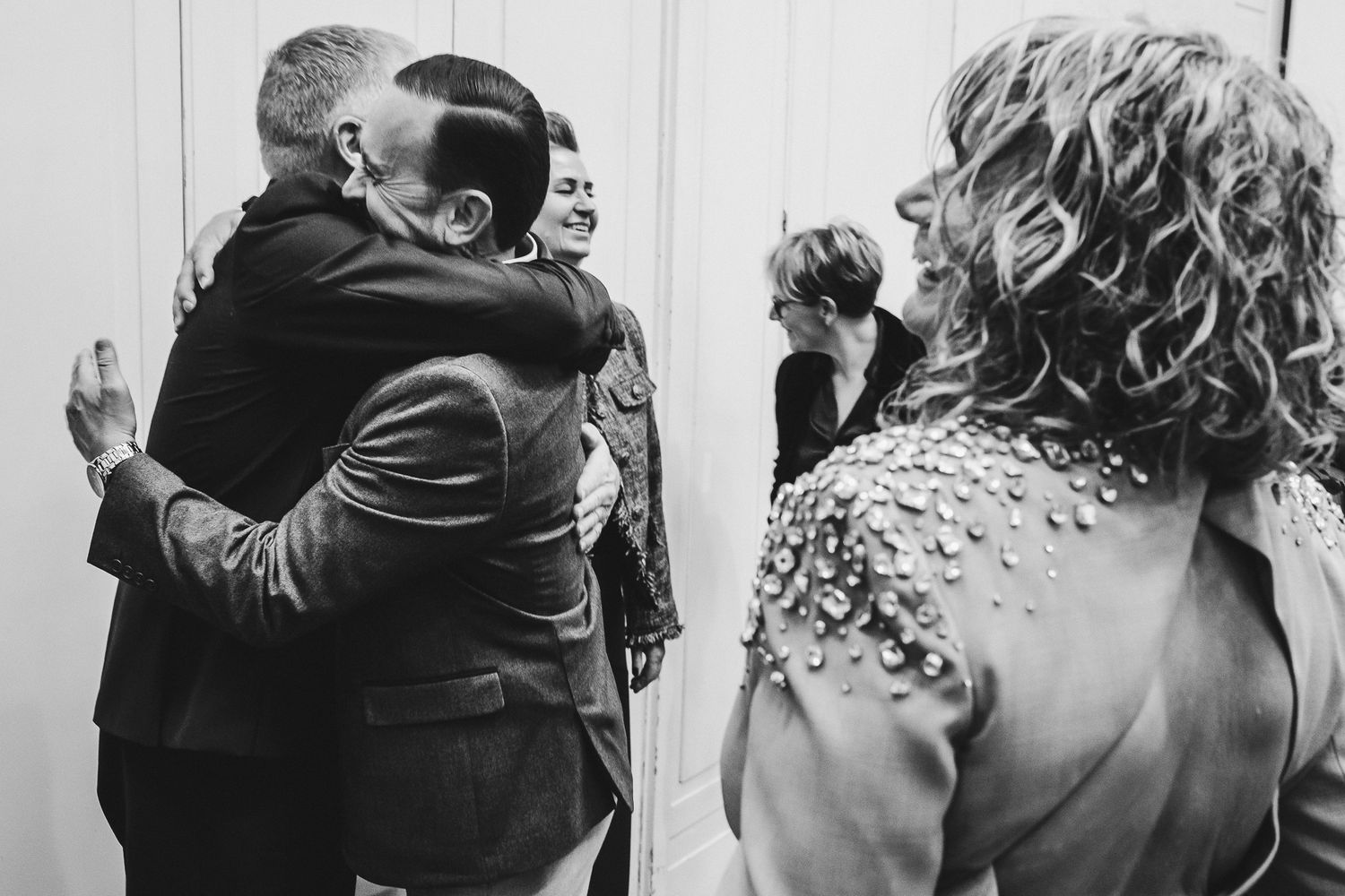 Black and white image of a wedding celebration with guests hugging and embracing.