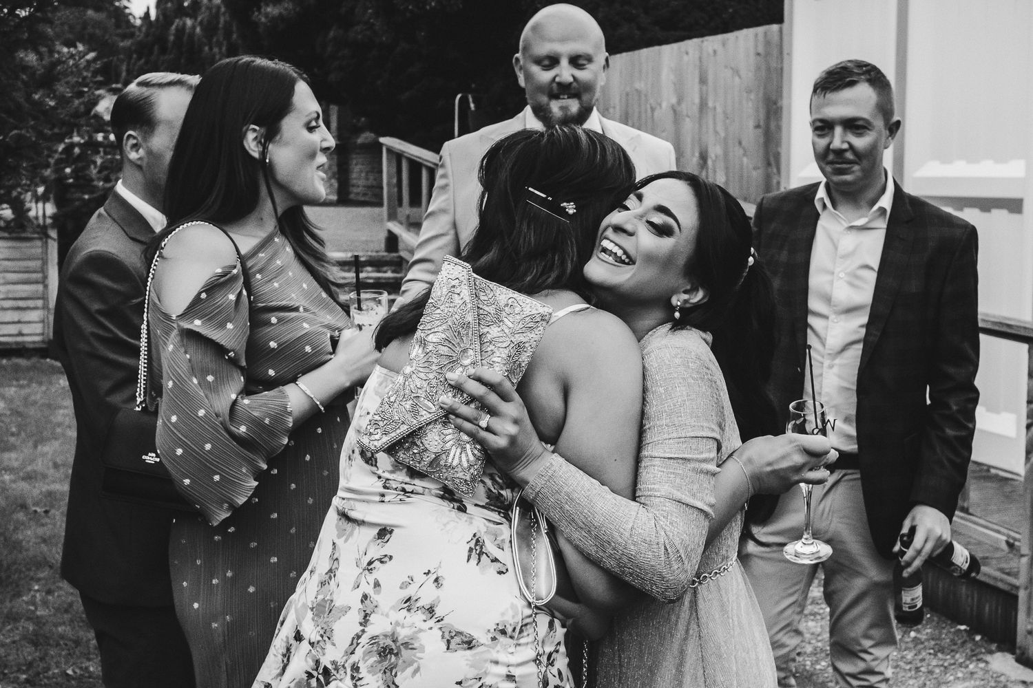 A group of guests gather and share laughs during a lively outdoor wedding celebration.