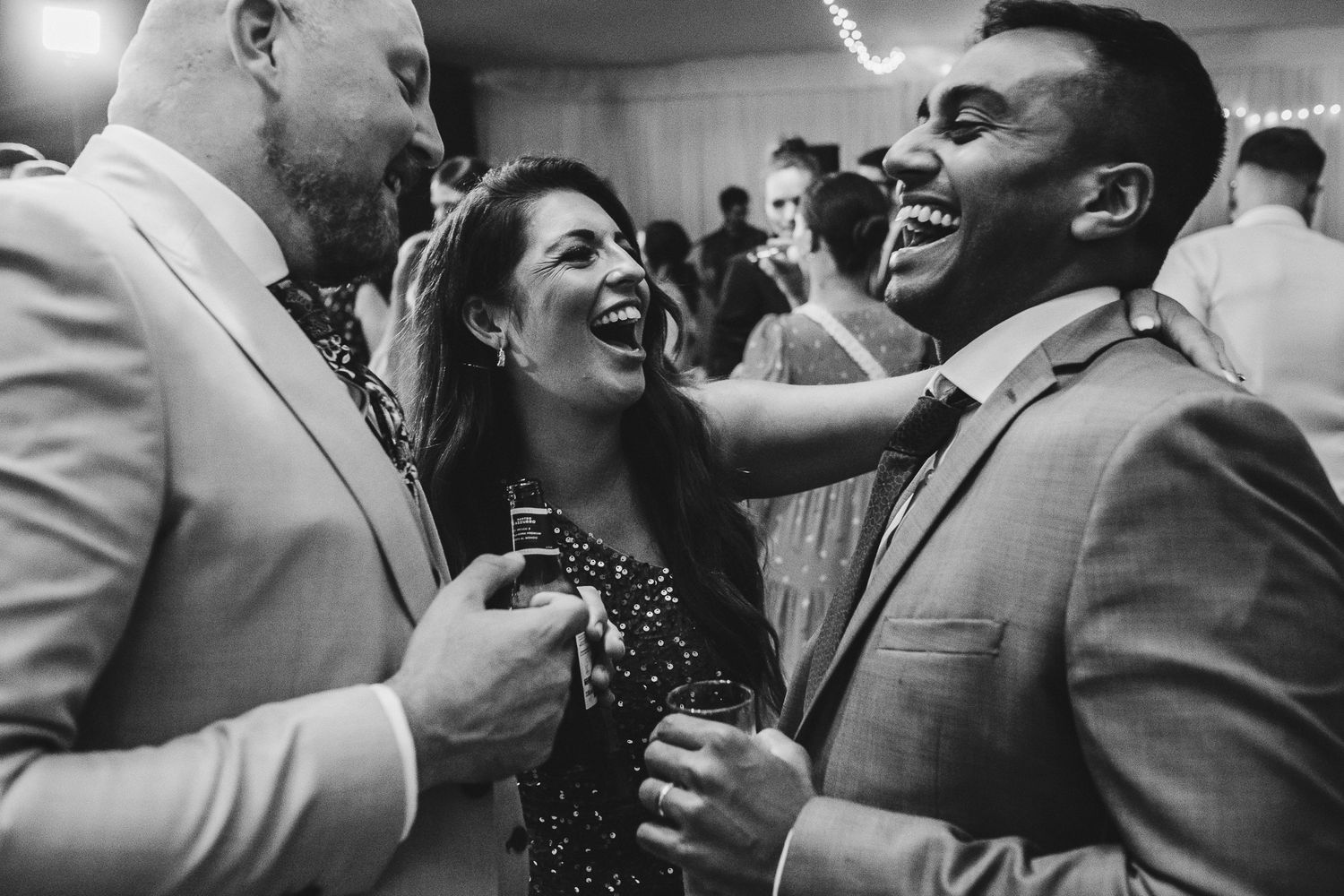 Three people sharing a joyous moment at a party, laughing together while holding drinks.