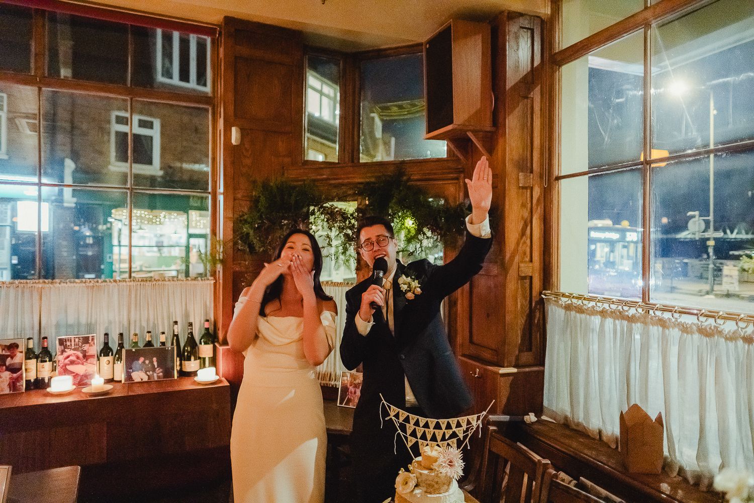 A candid moment at a wedding reception as the newlyweds laugh and share cake in a rustic wood-paneled venue.