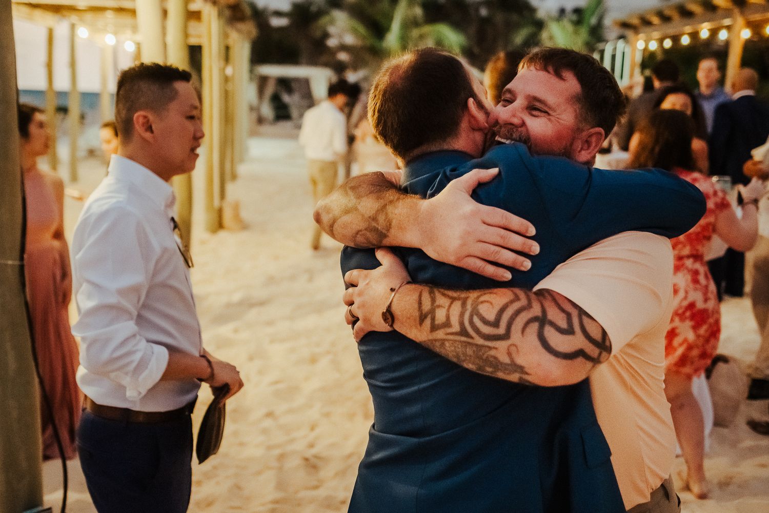 Sunset beach wedding reception photo showing guests sharing warm embraces.