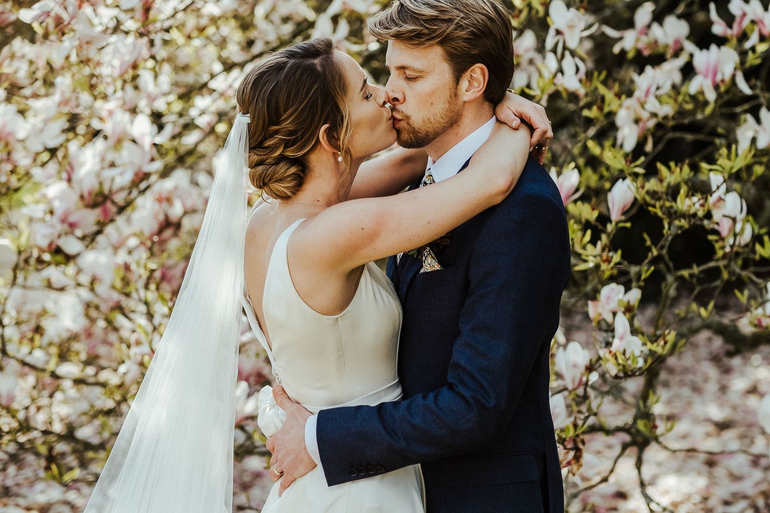 Wedding couple shares intimate moment under flowering trees during springtime photo session.