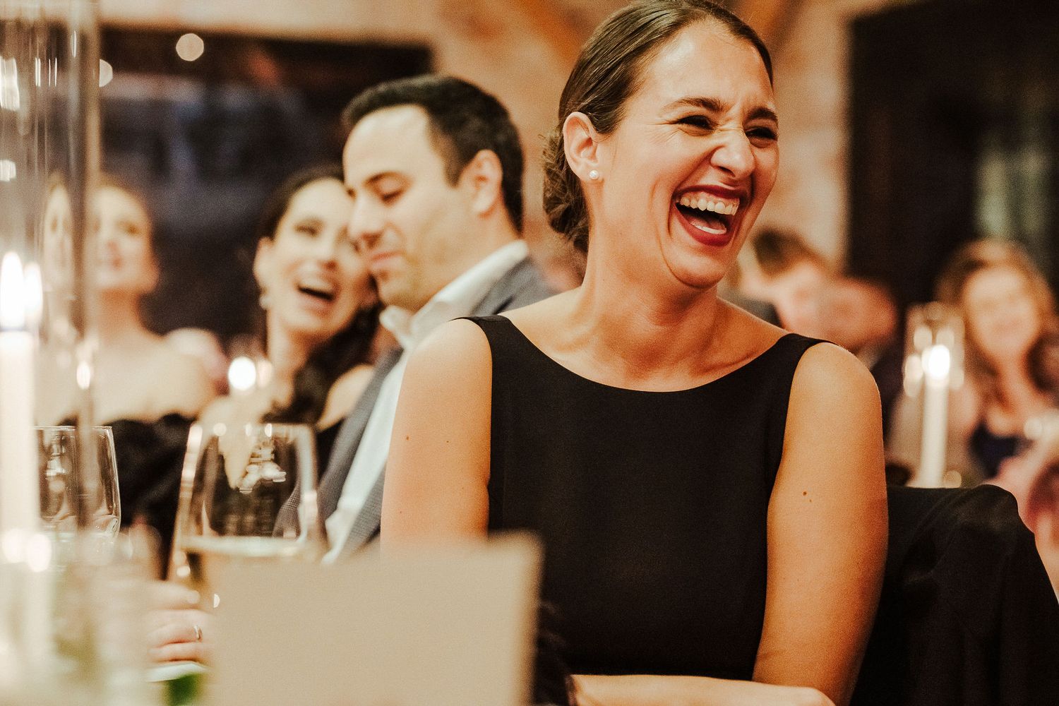 Wedding guests laugh joyfully during an elegant evening reception dinner.