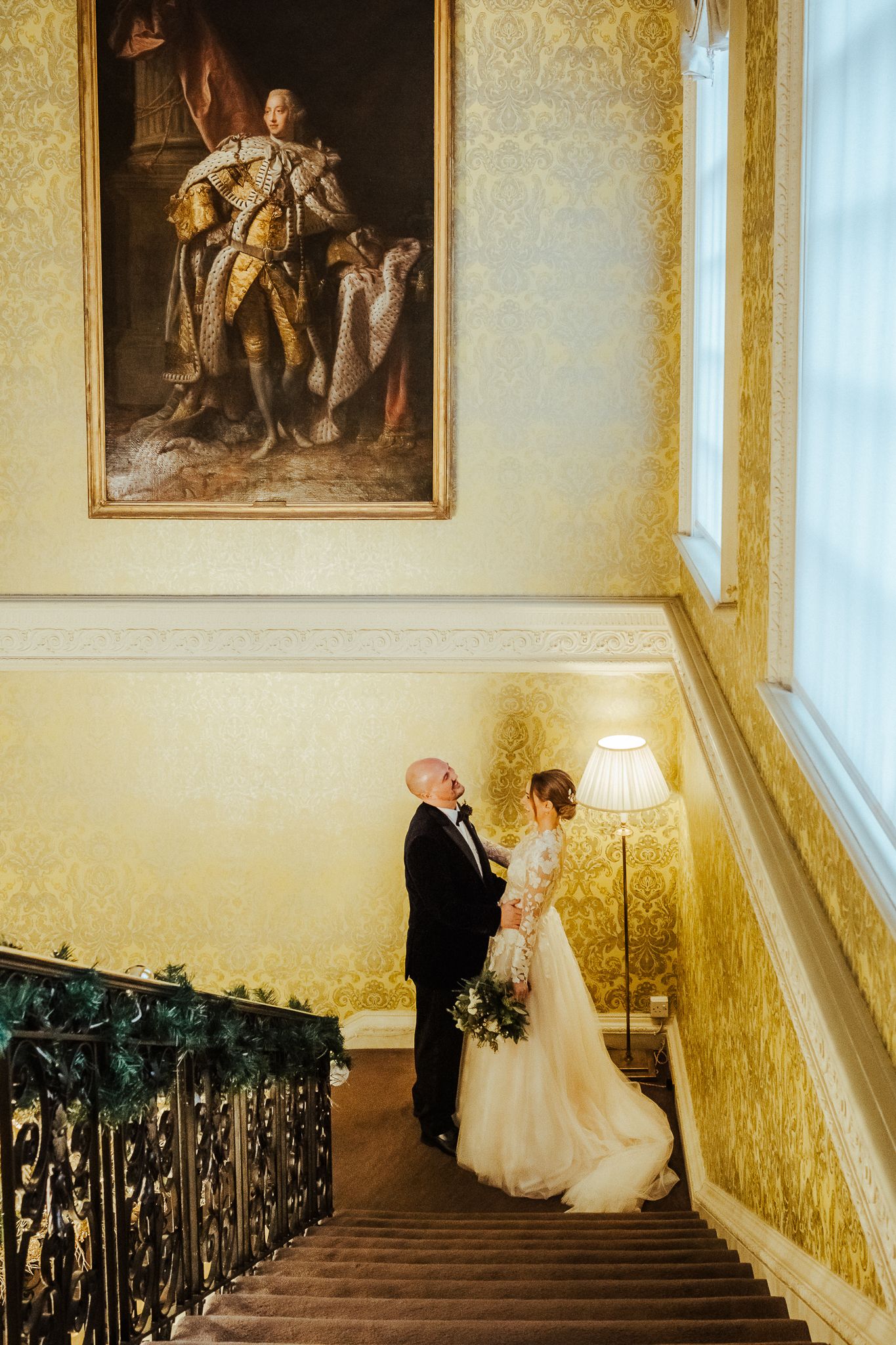 Elegant staircase wedding portrait with historic painting and ornate details.
