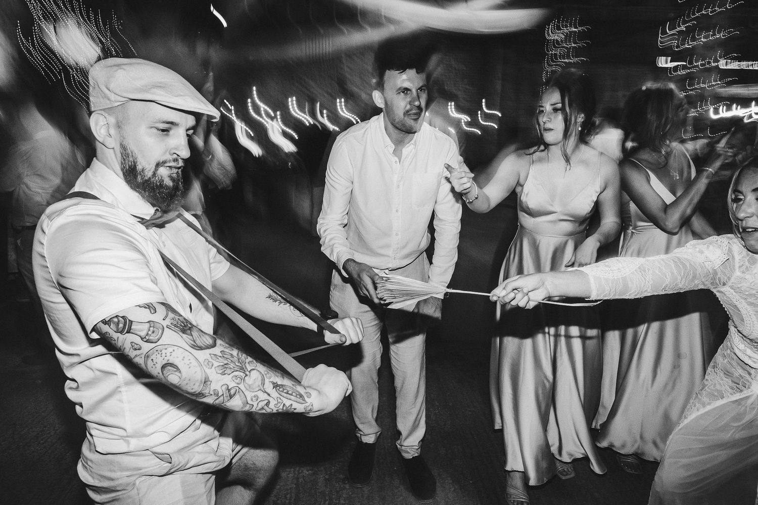 Black and white photo of wedding guests dancing in a line at a reception.