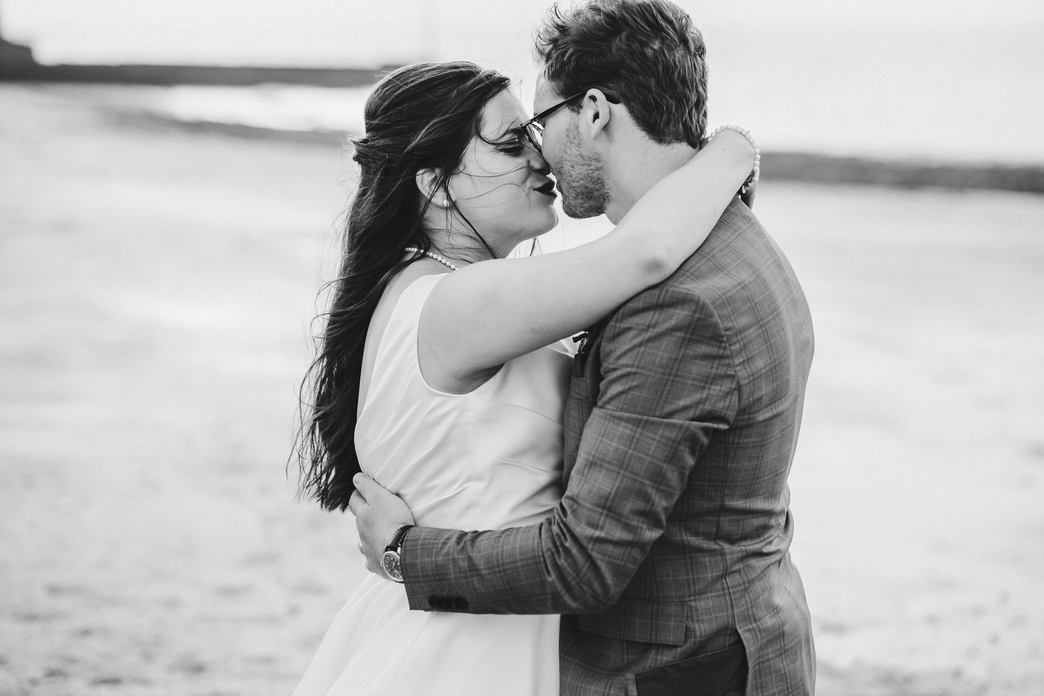 Intimate black and white portrait of a couple embracing on a beach.