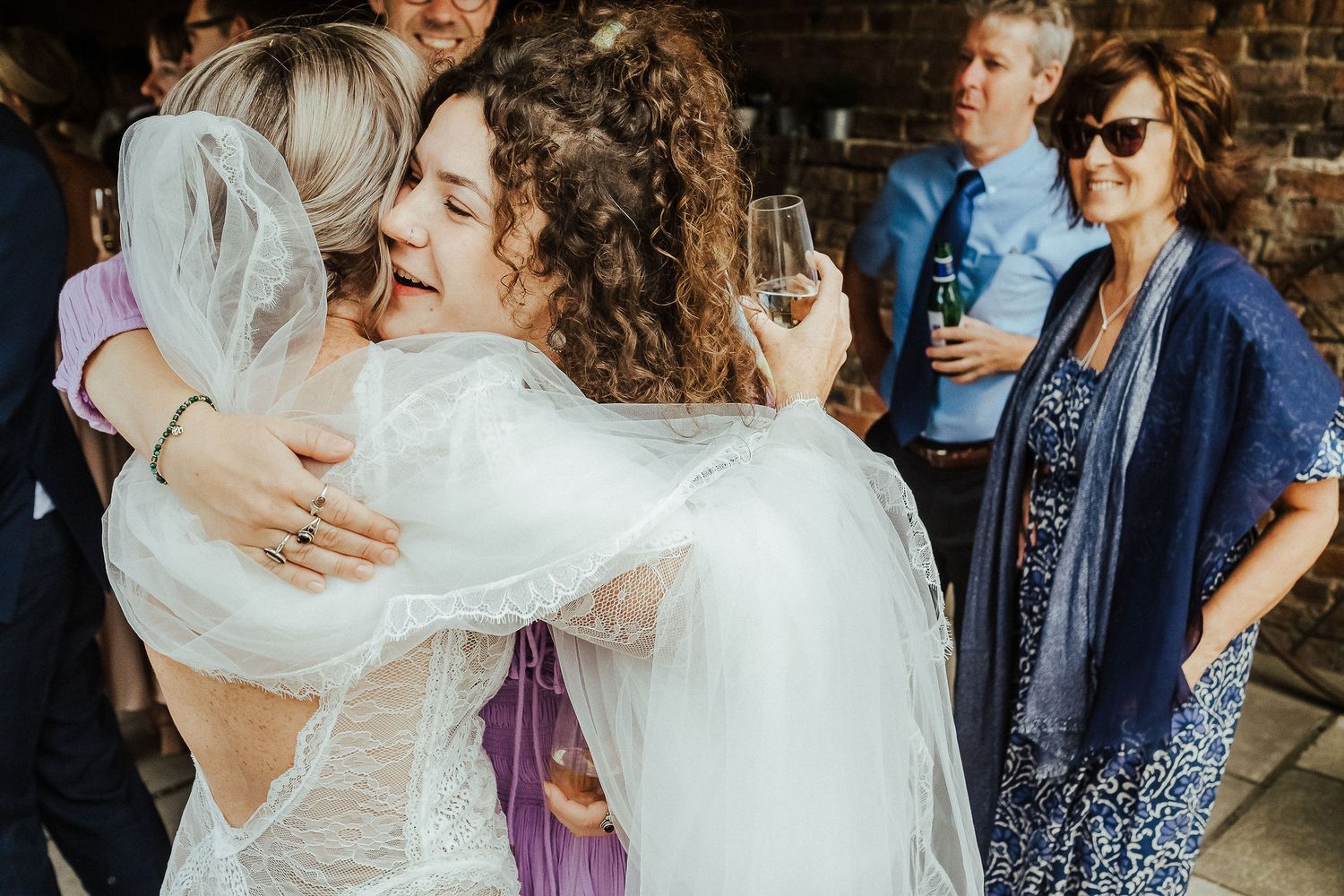 Wedding guests share warm hugs and embraces at rustic brick venue during celebration.