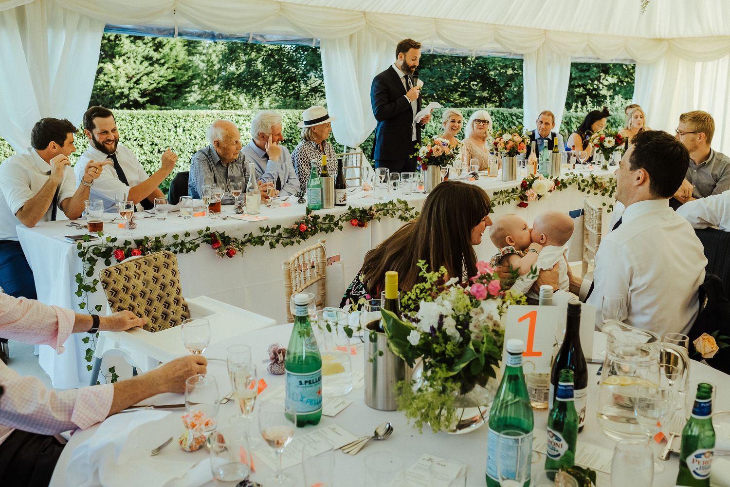 Wedding reception under white tent with decorated tables and floral centerpieces.