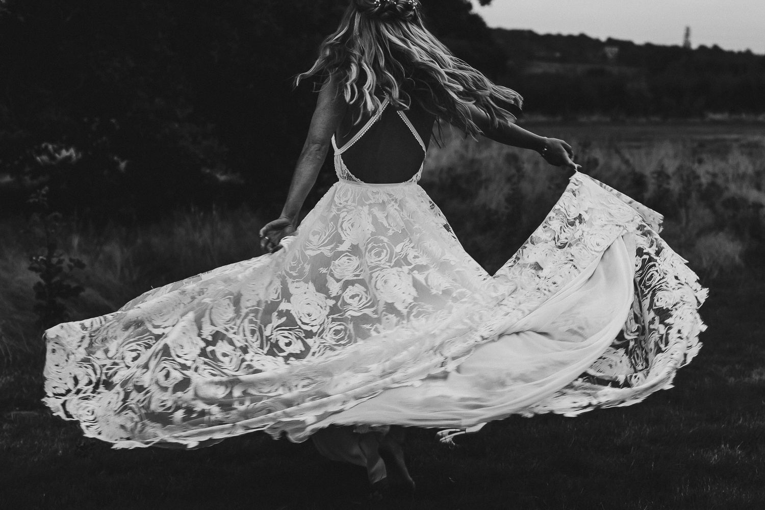 A flowing lace wedding dress train trails across dark ground creating an elegant pattern.