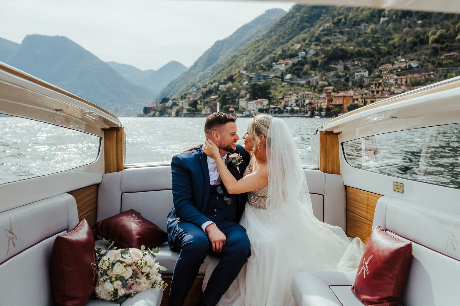 Newlyweds share an intimate moment on luxury boat with stunning mountain lake scenery.