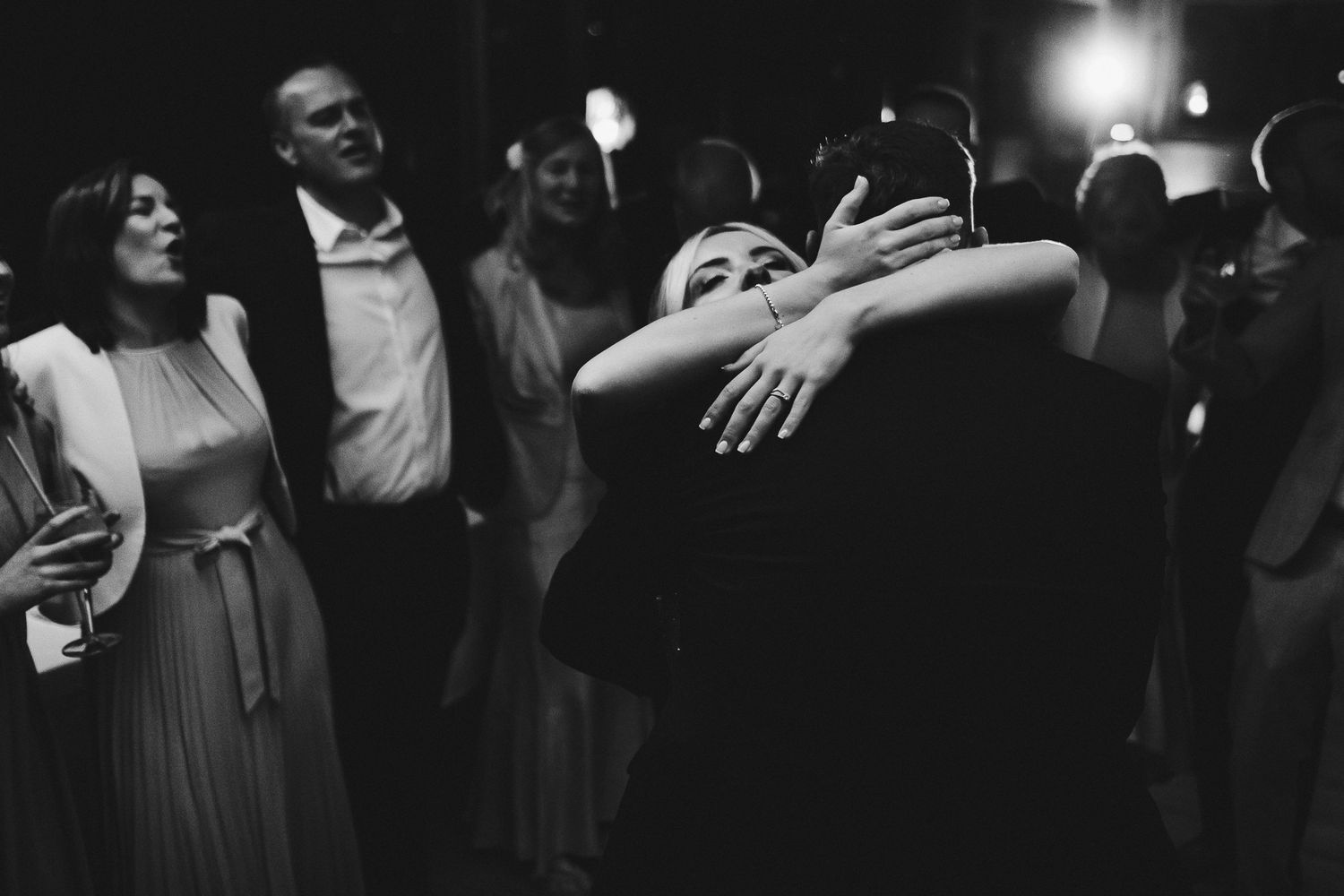 Black and white photo of wedding reception dancing with guests embracing.