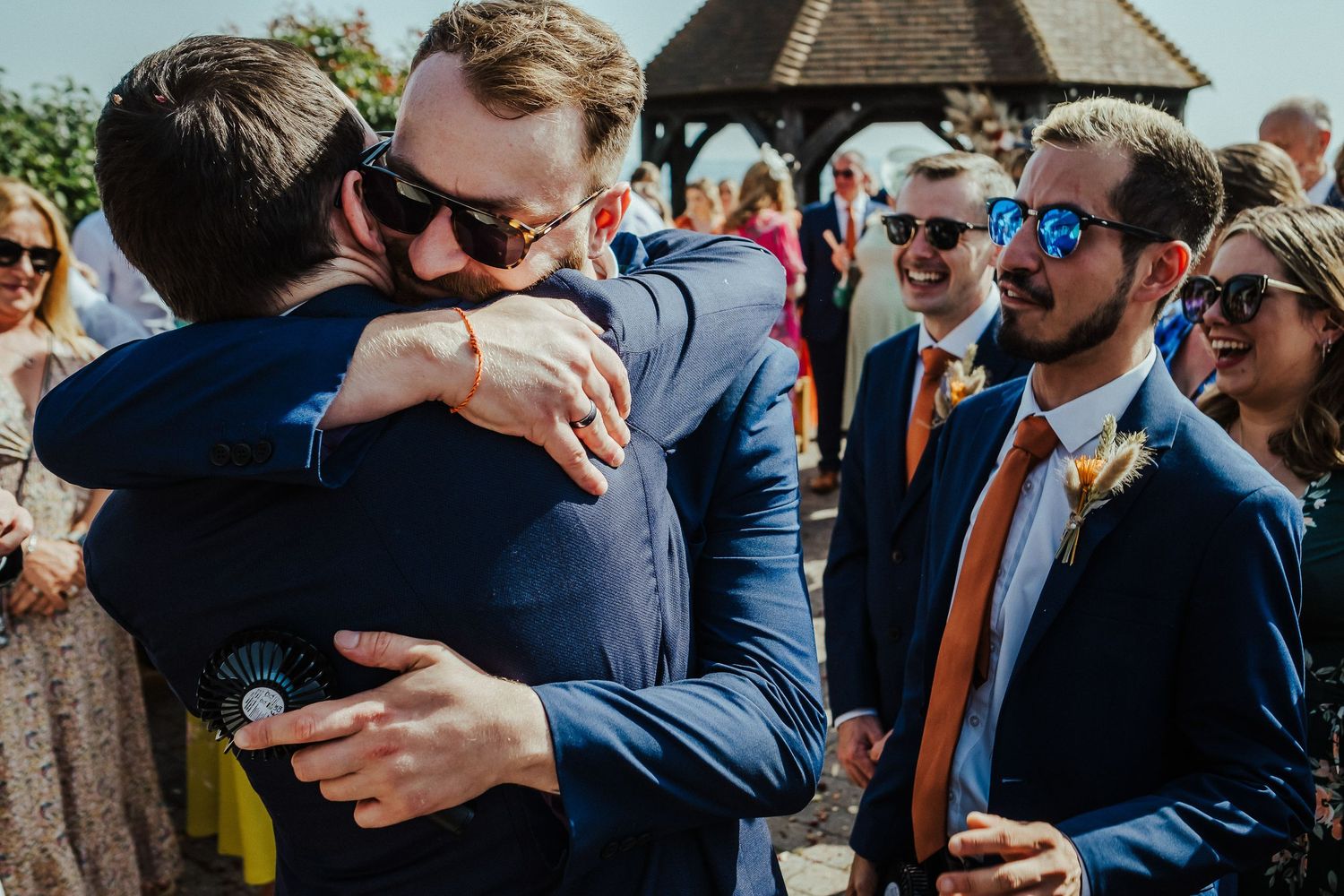 Emotional embrace between wedding guests during an outdoor celebration.