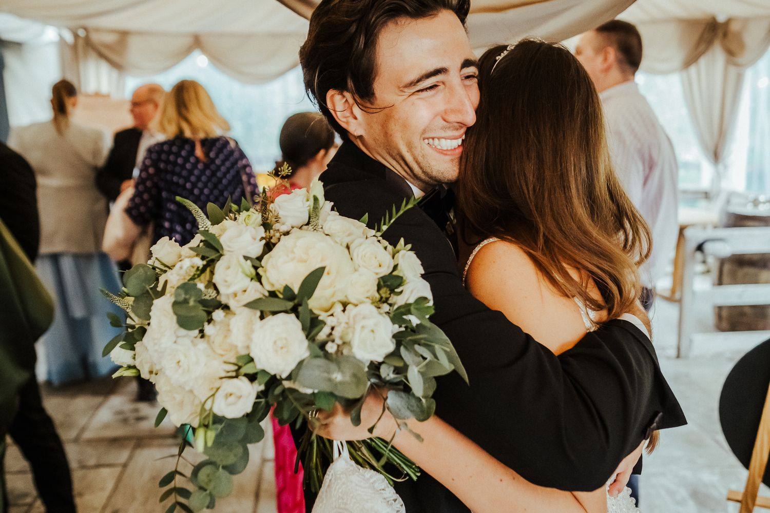 A joyful embrace with white roses at an indoor wedding celebration.