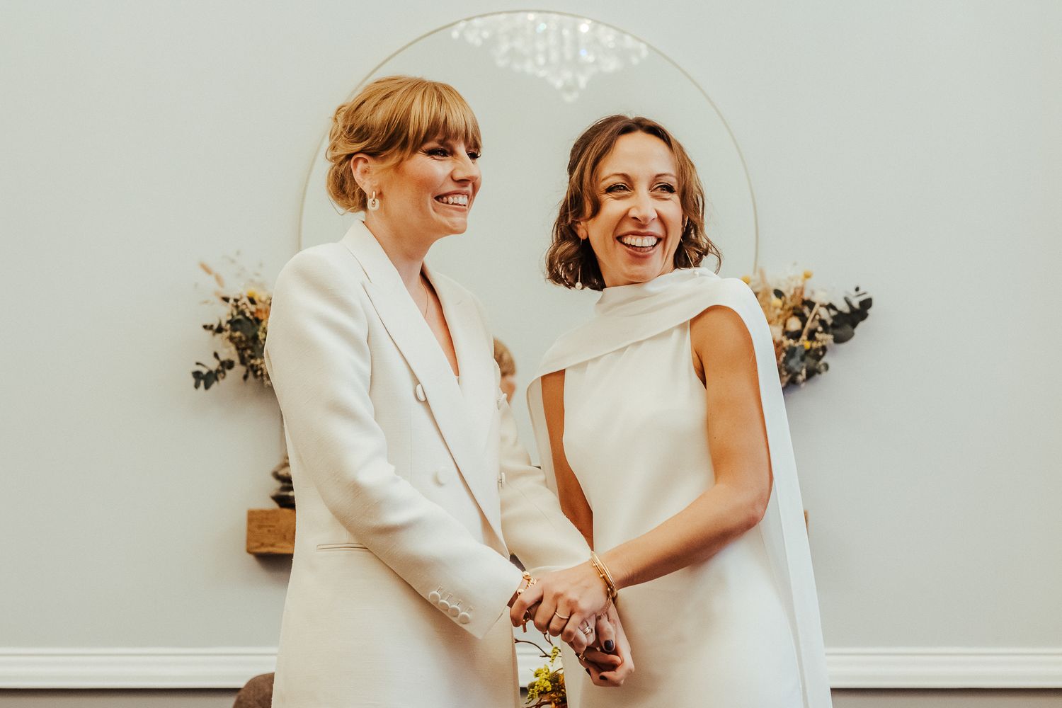 Joyful couple in white wedding attire sharing a tender moment against a light backdrop.