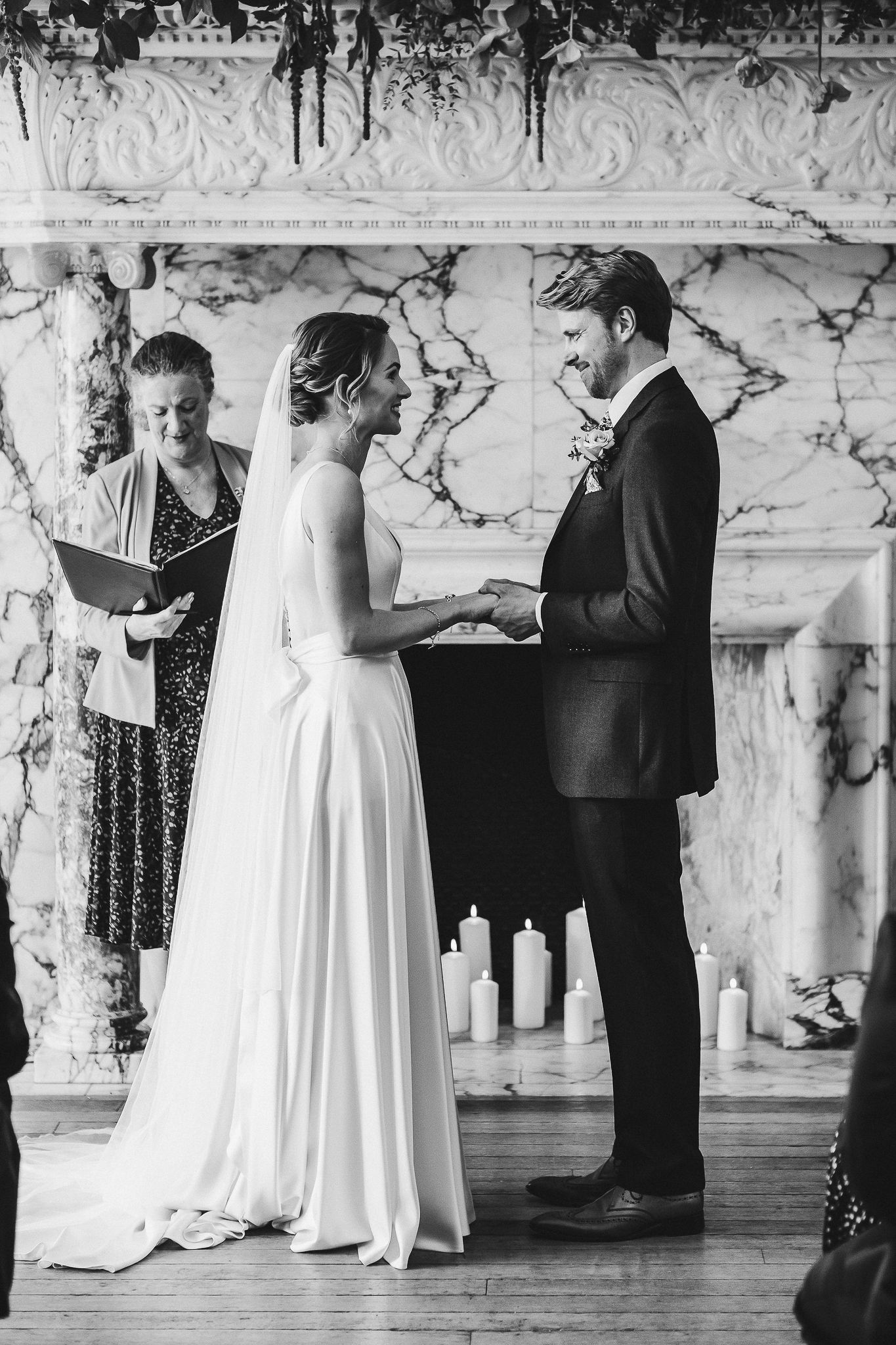 Black and white photo of wedding ceremony with couple and officiant against marble backdrop.