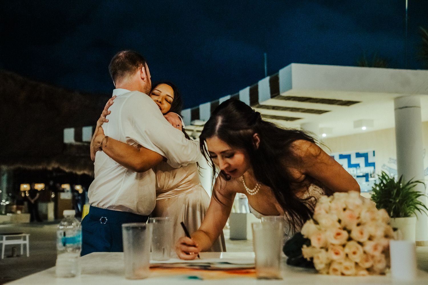 Wedding celebration guests lean over a table together during a joyous moment.