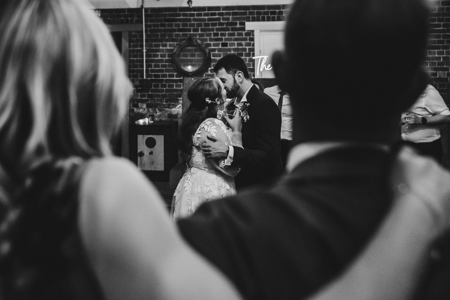 A candid black and white wedding moment captured through a crowd of guests watching the couple.