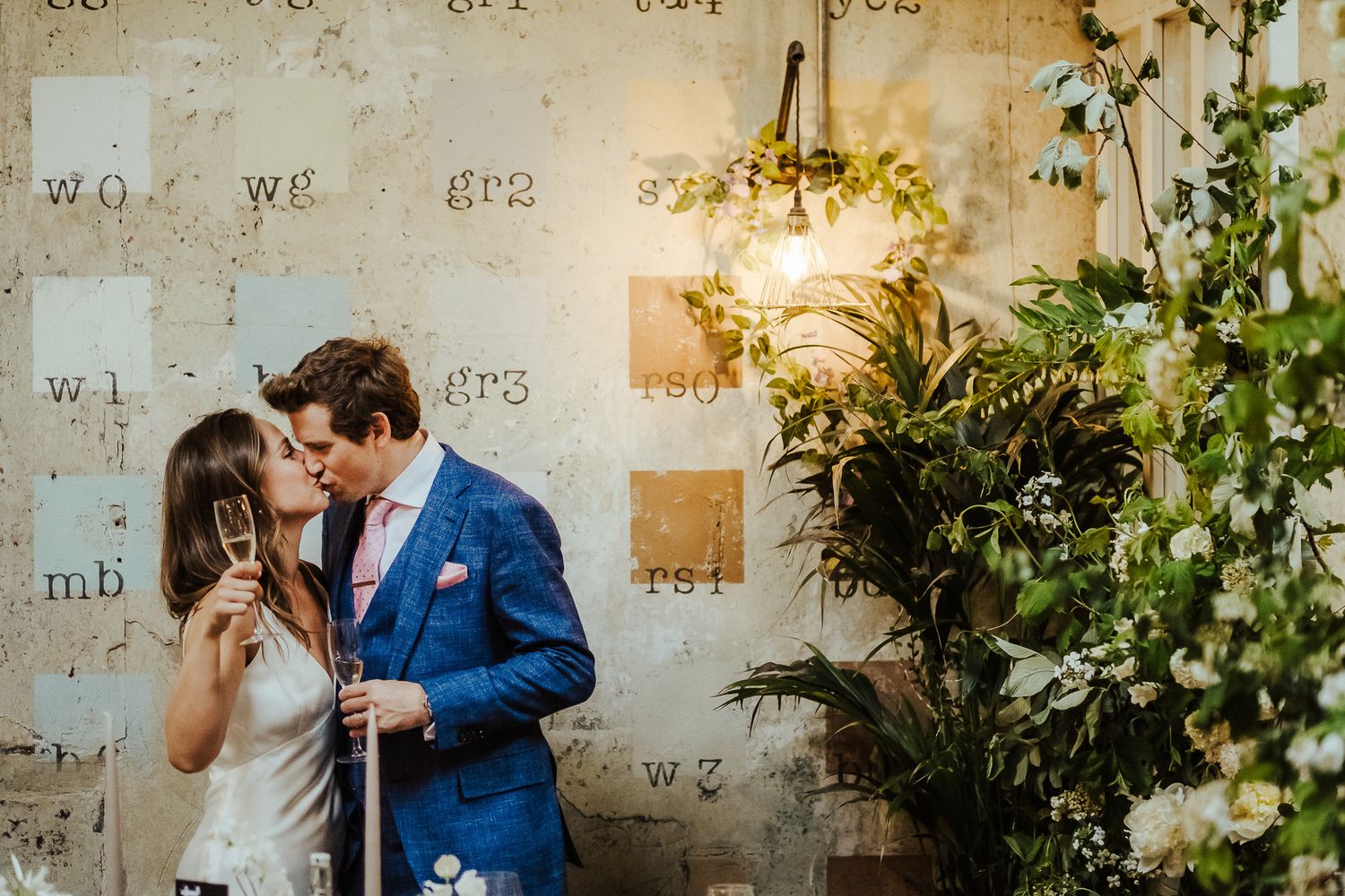 Romantic moment against an industrial wall with decorative plants and warm lighting.